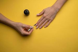 Close-up of a woman paints her nails with lacquer on a yellow background, top view photo