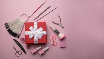 conjunto de herramientas y accesorios de manicura con caja de regalo roja sobre un fondo rosa. manicura de hardware, endecha plana. foto