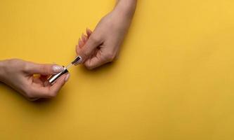 Close-up of a woman paints her nails with lacquer on a yellow background, top view photo