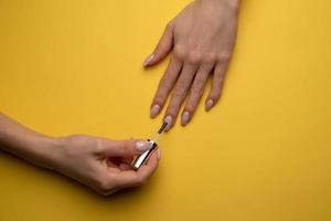 Close-up of a woman paints her nails with lacquer on a yellow background, top view photo