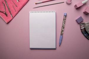Top view of open empty spiral notebook with pen and manicure accessories on pink background photo