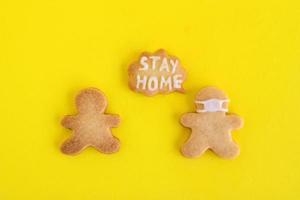 Galletas caseras de pan dulce con glaseado blanco sobre fondo amarillo, vista superior. dos hombres, uno de ellos con máscara facial y con una nube de llamadas con texto: quédese en casa. foto