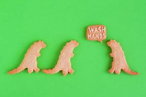 Homemade cookies in shapes of dinosaurs with inscription - Wash hands - on green background, top view. Sweet shortbread with white glaze. Social distancing concept. photo