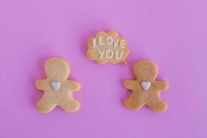 Homemade shortbread cookies with white glaze on pink background, top view. Two people with callout cloud with text - I love you photo