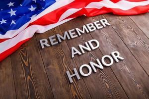 words remember and honor laid with silver metal letters on wooden background with USA flag above photo