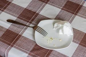 empty white dish with leftovers of eaten food, crumpled table-napkin and steel fork photo
