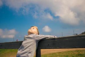 Small kid enjoying in sunlight while resting on a bench in nature. photo