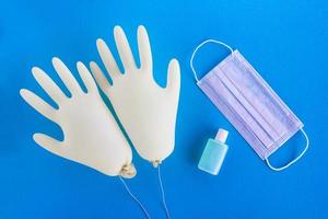 Pair of disposable medical gloves, face mask and hand sanitizer on blue background with copy space. Concept of new normal lifestyle. photo