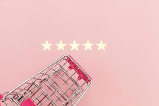 Small supermarket grocery push cart for shopping toy with wheels and 5 stars rating isolated on pastel pink background. Retail consumer buying online assessment and review concept. photo