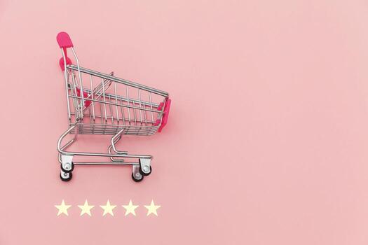 Small supermarket grocery push cart for shopping toy with wheels and 5 stars rating isolated on pastel pink background. Retail consumer buying online assessment and review concept. photo