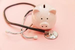 Medicine doctor equipment stethoscope and piggy bank isolated on pink pastel background. Health care financial checkup or saving for medical insurance costs concept. Copy space. photo