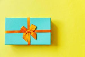 Christmas New Year birthday valentine celebration present romantic concept. Simply minimal design blue gift box isolated on yellow colorful background. Flat lay top view copy space. photo