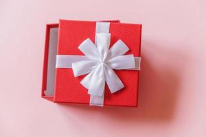 navidad año nuevo cumpleaños san valentín celebración presente concepto romántico. caja de regalo roja de diseño simplemente minimalista aislada sobre fondo de color rosa pastel. vista superior plana, espacio de copia foto