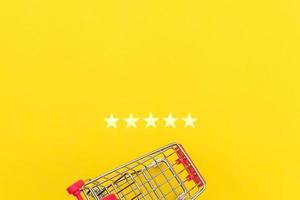 carrito de supermercado pequeño para comprar juguetes con ruedas y calificación de 5 estrellas aislado en fondo amarillo. concepto de evaluación y revisión en línea de compra de consumidores minoristas. foto