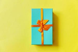 Christmas New Year birthday valentine celebration present romantic concept. Simply minimal design blue gift box isolated on yellow colorful background. Flat lay top view copy space. photo