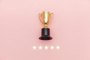 Simply flat lay design winner or champion gold trophy cup and 5 stars rating isolated on pink pastel background. Victory first place of competition. Winning or success concept. Top view copy space. photo