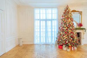 habitación interior clásica decorada en navidad, árbol de año nuevo con adornos rojos y dorados. moderno apartamento de diseño de interiores de estilo clásico blanco con chimenea y árbol de navidad. Nochebuena en casa. foto