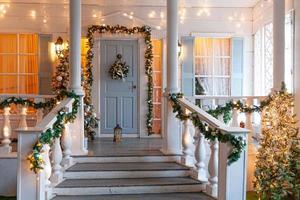 idea de decoración de porche de navidad. entrada de la casa decorada para vacaciones. guirnalda dorada y verde de ramas de abeto y luces en la barandilla. nochebuena en casa foto