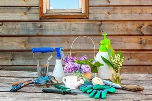 Gardening tools, watering can, shovel, spade, pruner, rake, glove, lilac, lily of the valley flowers on vintage wooden table. Spring or summer in garden, eco, nature, horticulture hobby concept. photo