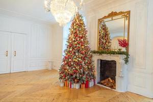 habitación interior clásica decorada en navidad, árbol de año nuevo con adornos rojos y dorados. moderno apartamento de diseño de interiores de estilo clásico blanco con chimenea y árbol de navidad. Nochebuena en casa. foto