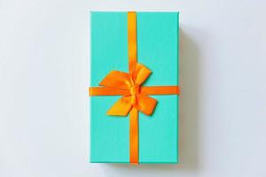 navidad año nuevo cumpleaños san valentín celebración presente concepto romántico. caja de regalo azul de diseño minimalista con cinta naranja aislada en fondo blanco. espacio de copia de vista superior plana. foto