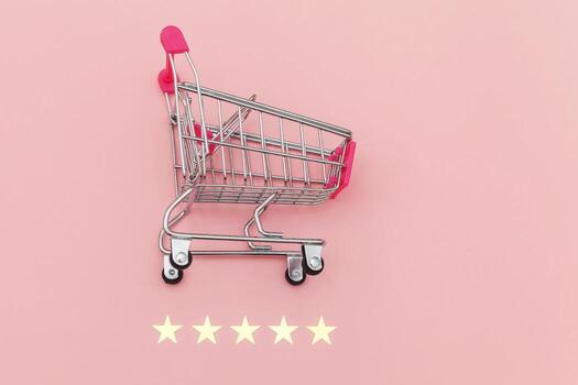 Small supermarket grocery push cart for shopping toy with wheels and 5 stars rating isolated on pastel pink background. Retail consumer buying online assessment and review concept. photo