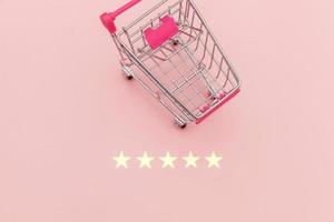 Small supermarket grocery push cart for shopping toy with wheels and 5 stars rating isolated on pastel pink background. Retail consumer buying online assessment and review concept. photo