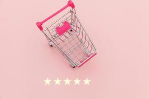 Small supermarket grocery push cart for shopping toy with wheels and 5 stars rating isolated on pastel pink background. Retail consumer buying online assessment and review concept. photo