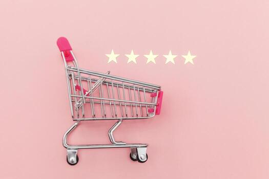 Small supermarket grocery push cart for shopping toy with wheels and 5 stars rating isolated on pastel pink background. Retail consumer buying online assessment and review concept. photo