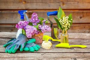 Gardening tools, watering can, shovel, spade, pruner, rake, glove, lilac, lily of the valley flowers on vintage wooden table. Spring or summer in garden, eco, nature, horticulture hobby concept. photo