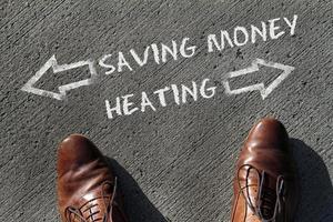 Person having to decide between Heating and Saving Money - top view of the words and arrows pointing in opposite directions photo