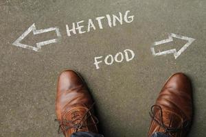 Person having to decide between Heating and Food - top view of the words and arrows pointing in opposite directions photo