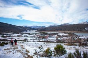 hikers walking through the snow between mountains with lake photo