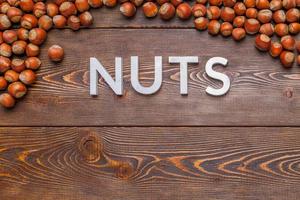 the word nuts laid with silver letters on wooden board background surrounded with hazelnuts photo