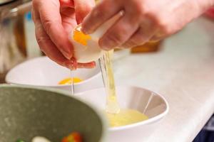 senior caucasian woman hands breaking white chicken egg above white bowl photo