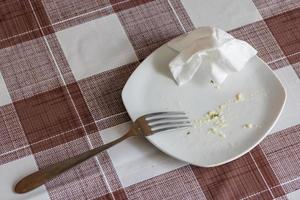 empty white dish with leftovers of eaten food, crumpled table-napkin and steel fork photo