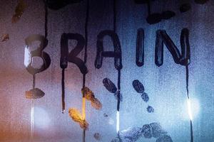 the word brain written on night wet window glass with palm prints close-up with blurred background photo