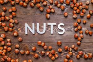 the word nuts laid with silver letters on wooden board background surrounded with scattered hazelnuts photo