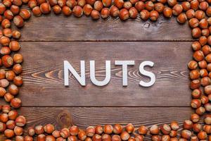 rectangular frame of many hazelnuts with shells on brown wooden surface with word nuts laid with silver letters photo