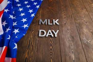 la palabra mlk day colocada con letras de metal plateado sobre una superficie de madera con una bandera de estados unidos arrugada en el lado izquierdo foto