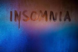 word insomnia handwritten on night wet window glass close-up photo