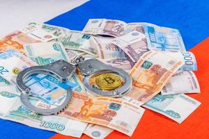 russian paper rubles currency and bitcoin shiner chained with handcuffs on russian flag background photo