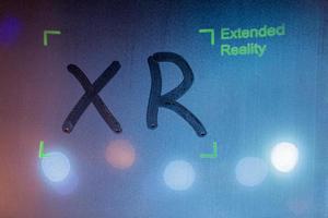 the word xr handwritten by finger on wet window glass with green overlay with words extended reality and corner frame photo