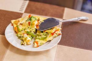 plate with slices of omelet of scrambled eggs with vegetables and stainless steel spatula photo