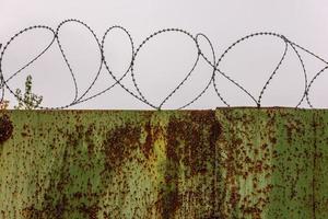 flat rusted sheet metal fence with peeled off green paint and barbed wire on top of it photo