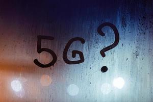 the question 5G written by finger on wet glass with blurred lights in background photo