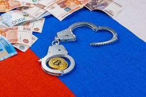 russian paper rubles currency and bitcoin shiner chained with handcuffs on russian flag background photo