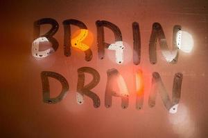 Las palabras fuga de cerebros escritas en el primer plano de cristal de la ventana húmeda nocturna con fondo borroso en colores naranja foto