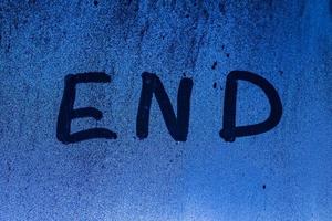 The word end written on night sweaty window glass with blurred blue light in the background photo