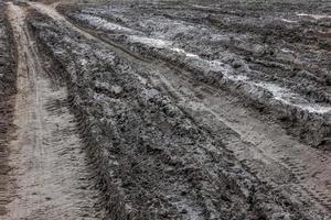 A broken rural country road after the rain. Puddles after rain on a dirt road. Clay, soil and puddles at cloudy day light after rain, autumn season. photo